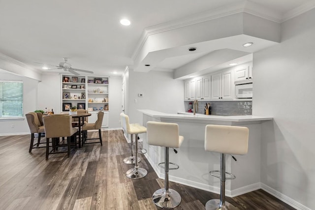 2807 Round Table Rd, Austin, TX 78746 - kitchen featuring white microwave, crown molding, a breakfast bar area, white cabinetry, and dark wood finished floors