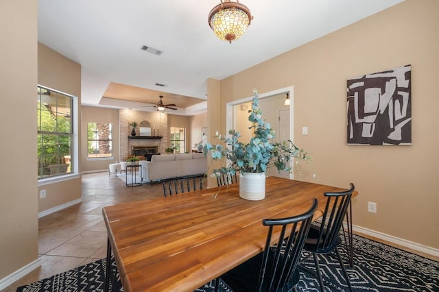 314 Hurst Creek Rd, Lakeway, TX 78734 - tiled dining space with baseboards, a large fireplace, a ceiling fan, and a raised ceiling