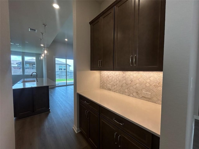 8217 Grenadier Dr, Austin, TX 78738 - kitchen featuring dark wood-type flooring, tasteful backsplash, light countertops, dark brown cabinets, and pendant lighting