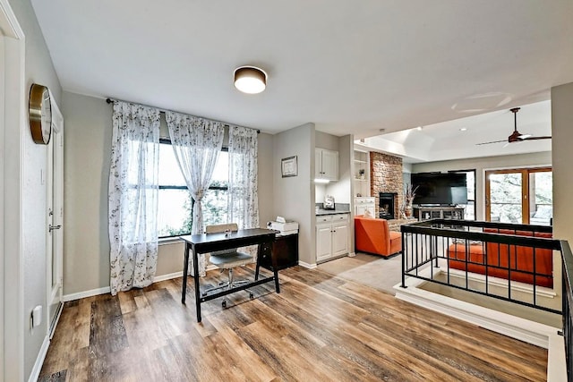 409 Hurst Creek Rd, Lakeway, TX 78734 - kitchen featuring light wood-type flooring, a large fireplace, ceiling fan, baseboards, and white cabinetry