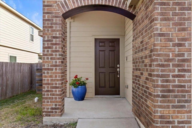 view of exterior entry with fence and brick siding