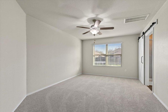 unfurnished bedroom with a barn door, visible vents, carpet flooring, and baseboards