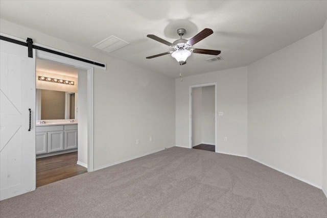 unfurnished room with a barn door, dark carpet, visible vents, a ceiling fan, and baseboards