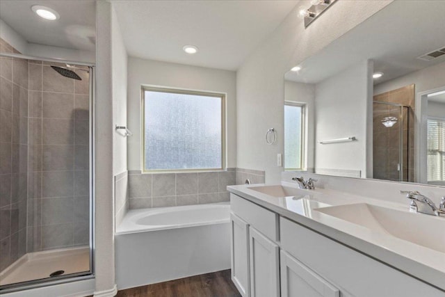 bathroom with wood finished floors, a sink, a stall shower, a wealth of natural light, and visible vents