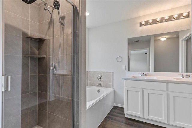 full bath with double vanity, wood finished floors, a sink, a bath, and a stall shower