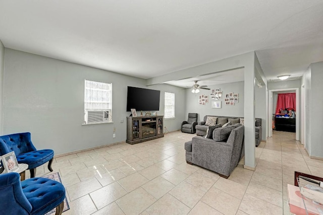 living area featuring light tile patterned floors, baseboards, a ceiling fan, and a glass covered fireplace