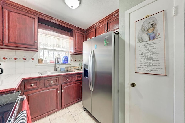 kitchen with stainless steel fridge, light tile patterned floors, stove, a sink, and reddish brown cabinets