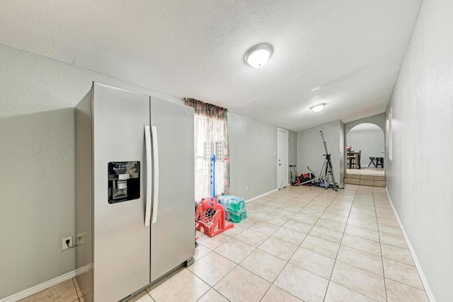 workout room featuring arched walkways, light tile patterned flooring, baseboards, and a textured ceiling