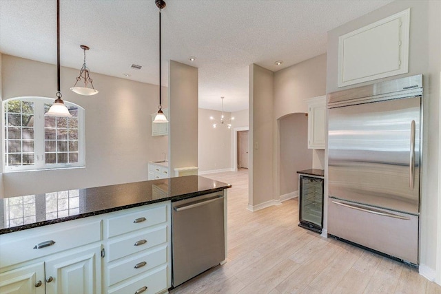 7304 Halbert Dr, Austin, TX 78750 - kitchen featuring stainless steel appliances, wine cooler, light wood-style flooring, arched walkways, and a textured ceiling
