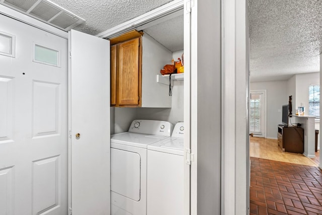 2110 Rio Grande St Unit 207, Austin, TX 78705 - laundry area with brick flooring, cabinet space, washing machine and clothes dryer, a textured ceiling, and baseboards
