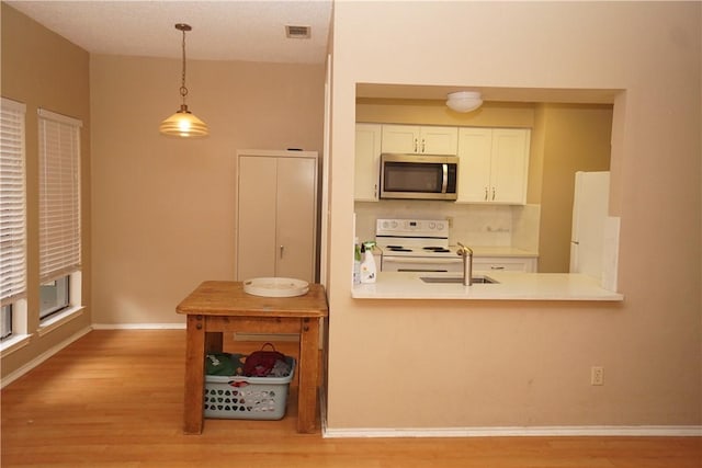 2706 Salado St Unit 210, Austin, TX 78705 - kitchen with stainless steel microwave, electric stove, light wood-style flooring, white cabinets, and backsplash