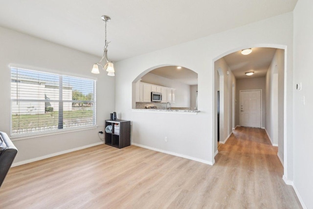 211 Almquist St, Hutto, TX 78634 - kitchen with light wood-style flooring, white cabinetry, stainless steel microwave, decorative light fixtures, and light countertops