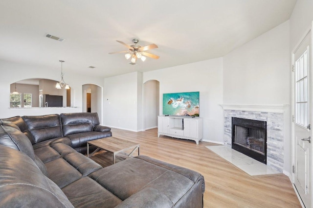 211 Almquist St, Hutto, TX 78634 - living area featuring arched walkways, light wood finished floors, a ceiling fan, a stone fireplace, and plenty of natural light
