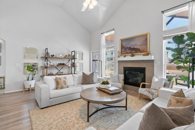 living area featuring high vaulted ceiling, ceiling fan, a fireplace, and light wood-style flooring