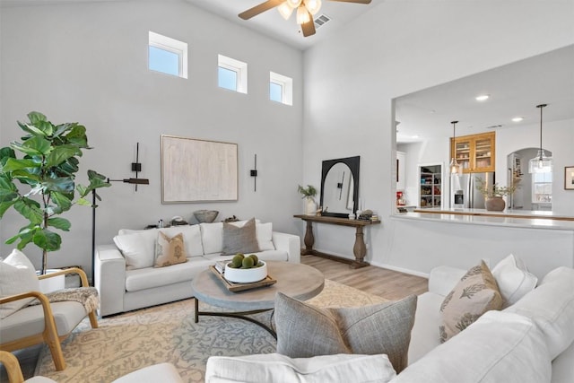 living room featuring ceiling fan, a high ceiling, recessed lighting, arched walkways, and light wood-style flooring