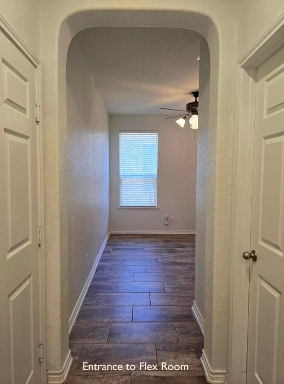 hall featuring arched walkways, baseboards, and wood finished floors