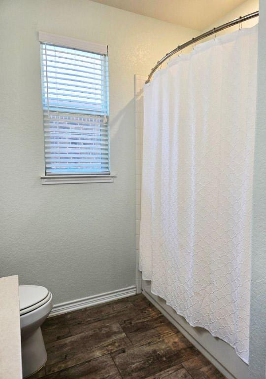 full bath featuring toilet, wood finished floors, shower / tub combo with curtain, and baseboards