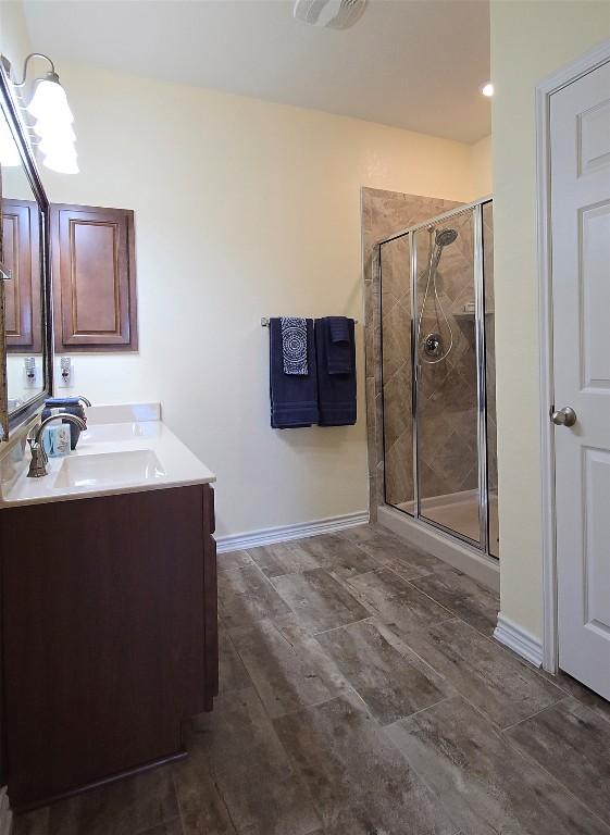 full bathroom featuring a stall shower, double vanity, baseboards, and a sink