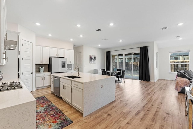 2233 Bravo Pass, Leander, TX 78641 - kitchen with a sink, appliances with stainless steel finishes, light wood finished floors, open floor plan, and white cabinetry