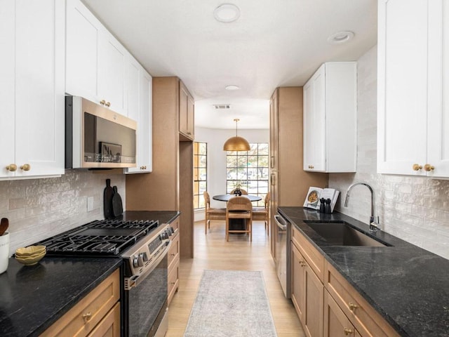 kitchen featuring a sink, white cabinetry, light wood-type flooring, stainless steel appliances, and dark stone counters