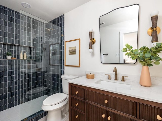 bathroom with toilet, a tile shower, and vanity