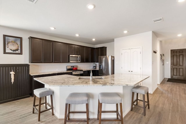 277 Biscayne Bay Bnd, Kyle, TX 78640 - kitchen with stainless steel appliances, light wood finished floors, dark brown cabinetry, a breakfast bar area, and recessed lighting