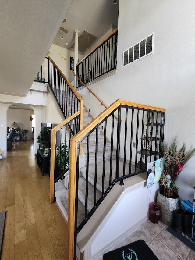 staircase featuring arched walkways, wood finished floors, and a towering ceiling