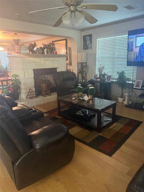 living room featuring visible vents, wood finished floors, a stone fireplace, ceiling fan, and arched walkways