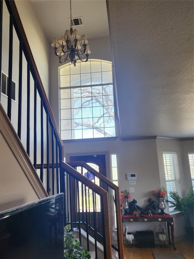 foyer entrance with a high ceiling, a textured ceiling, a chandelier, stairs, and visible vents