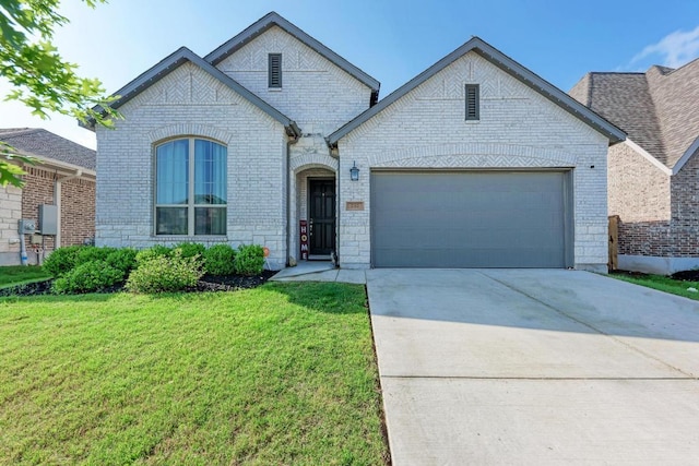 french country style house featuring brick siding, an attached garage, a front yard, and concrete driveway