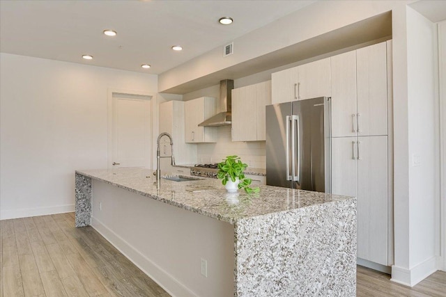 1715 Enfield Rd Unit 302, Austin, TX 78703 - kitchen with wall chimney exhaust hood, freestanding refrigerator, light wood-style floors, a kitchen island with sink, and light stone countertops