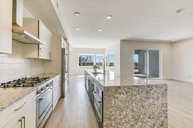 1715 Enfield Rd Unit 302, Austin, TX 78703 - kitchen with wall chimney exhaust hood, stainless steel appliances, light wood finished floors, an island with sink, and backsplash