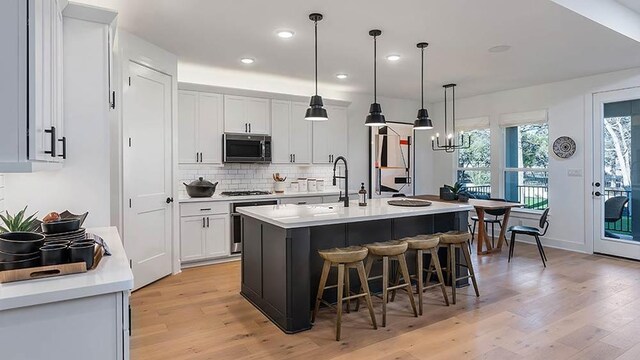 309 Golden Sage Ave, Georgetown, TX 78633 - kitchen with stainless steel appliances, light wood-style floors, decorative backsplash, a breakfast bar, and white cabinetry