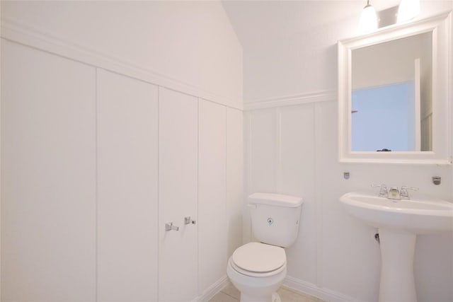 half bathroom with a decorative wall, toilet, and wainscoting