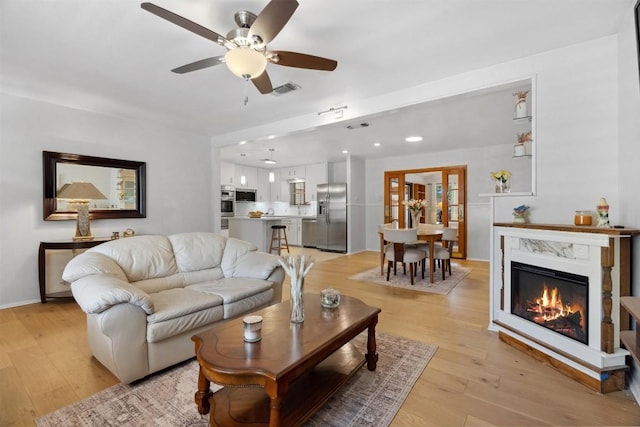 living room featuring visible vents, a fireplace, light wood-style floors, and ceiling fan