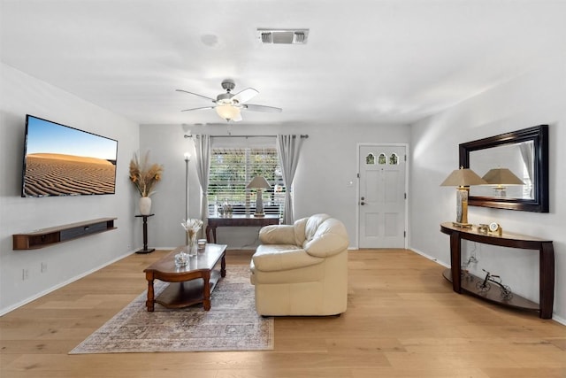 living room featuring light wood-type flooring, visible vents, a ceiling fan, and baseboards