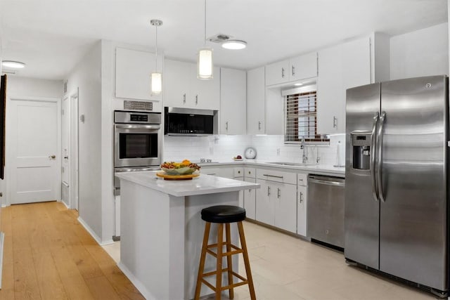 kitchen featuring white cabinets, light countertops, a sink, decorative backsplash, and appliances with stainless steel finishes