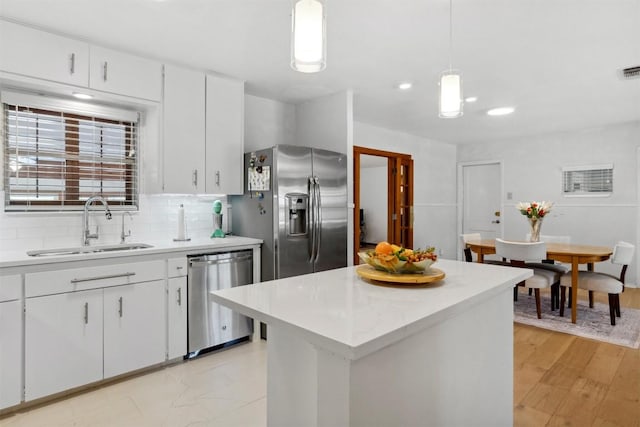 kitchen with a sink, light countertops, white cabinets, backsplash, and appliances with stainless steel finishes