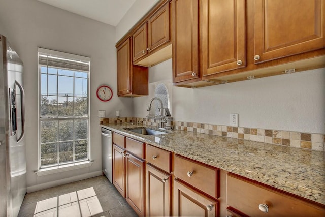 kitchen featuring a sink, stainless steel appliances, light stone counters, brown cabinetry, and light tile patterned floors