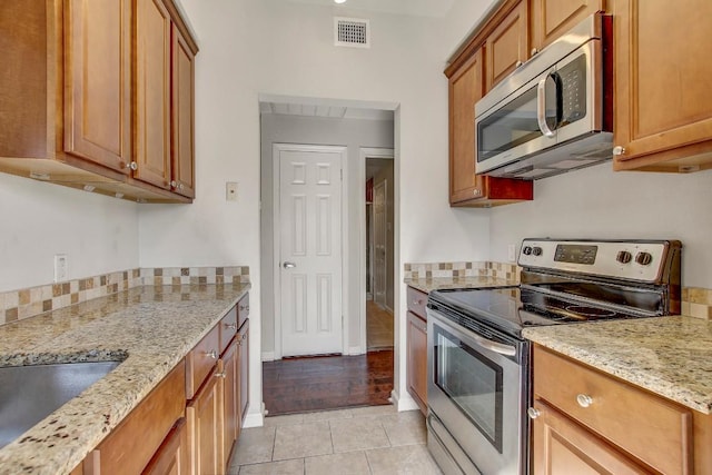 kitchen with appliances with stainless steel finishes, light tile patterned floors, light stone countertops, brown cabinets, and a sink