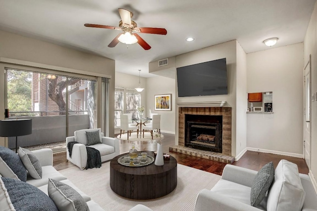 living area featuring wood finished floors, baseboards, a ceiling fan, recessed lighting, and a brick fireplace