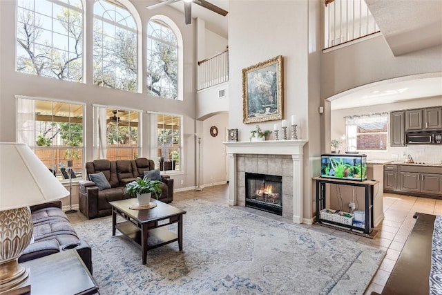 2535 Crenshaw Dr, Round Rock, TX 78664 - living area with ceiling fan, a towering ceiling, arched walkways, a tiled fireplace, and baseboards