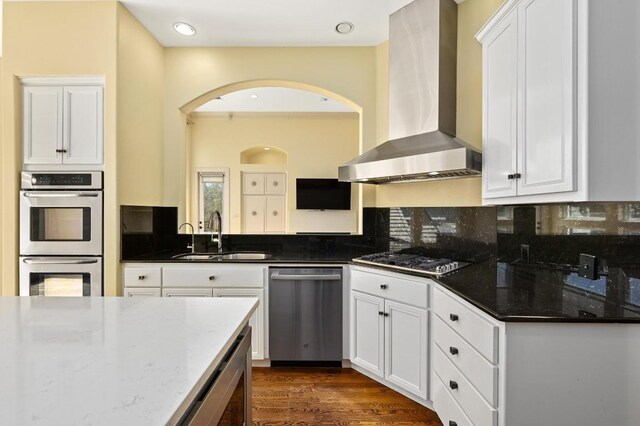 5903 Cane Pace, Austin, TX 78746 - kitchen featuring wall chimney exhaust hood, appliances with stainless steel finishes, a sink, arched walkways, and dark stone counters