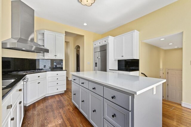 5903 Cane Pace, Austin, TX 78746 - kitchen with wall chimney range hood, stainless steel appliances, arched walkways, tasteful backsplash, and dark wood-type flooring
