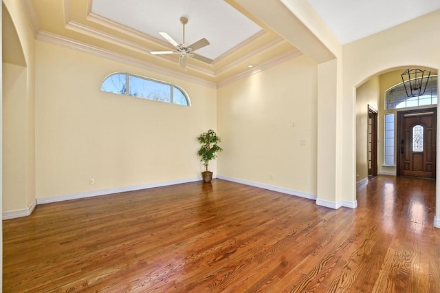 entrance foyer with crown molding, ceiling fan, a tray ceiling, arched walkways, and wood finished floors