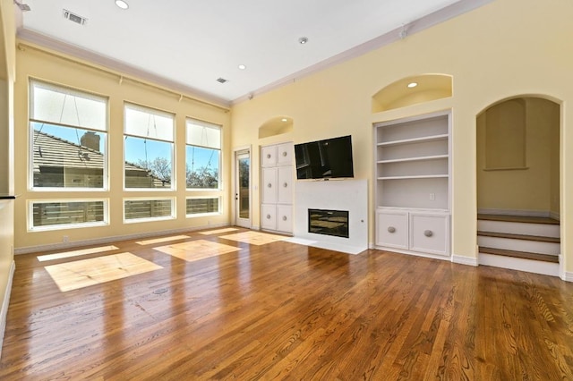 5903 Cane Pace, Austin, TX 78746 - unfurnished living room featuring built in shelves, wood finished floors, a glass covered fireplace, crown molding, and baseboards
