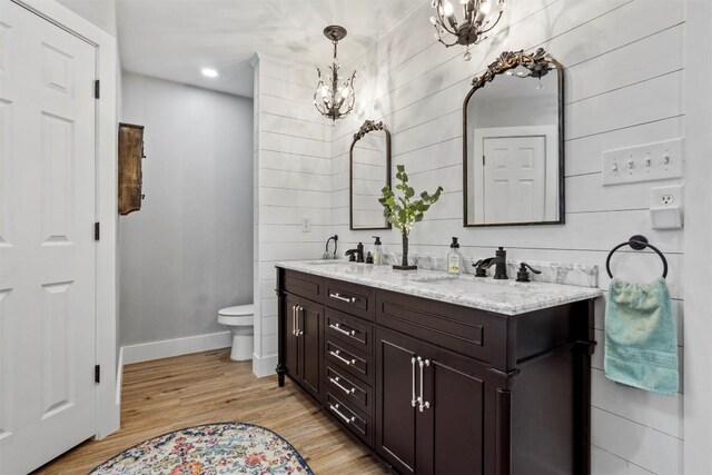bathroom featuring a chandelier, toilet, wood finished floors, a sink, and double vanity