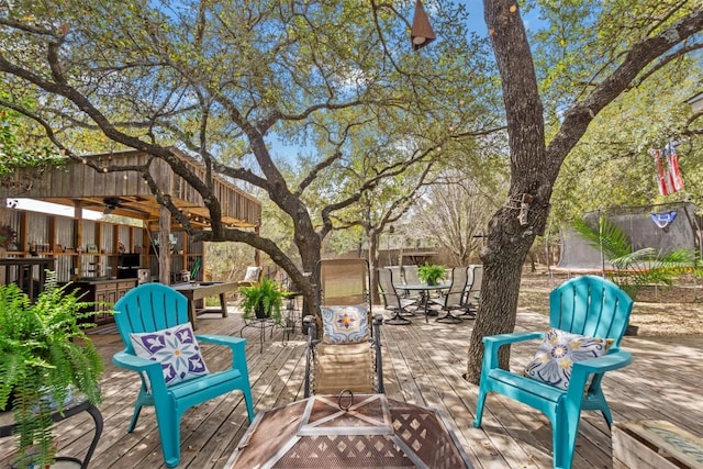 view of patio featuring a trampoline, a ceiling fan, outdoor dining space, fence, and a wooden deck