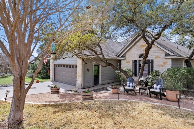 obstructed view of property featuring a garage, a shingled roof, a front yard, stone siding, and driveway
