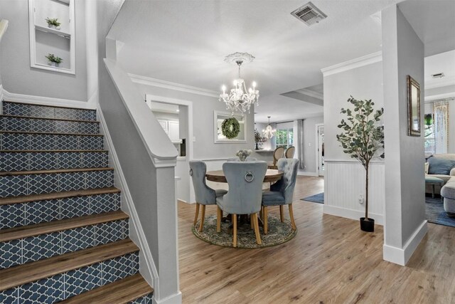 dining room featuring crown molding, visible vents, stairway, a chandelier, and wood finished floors